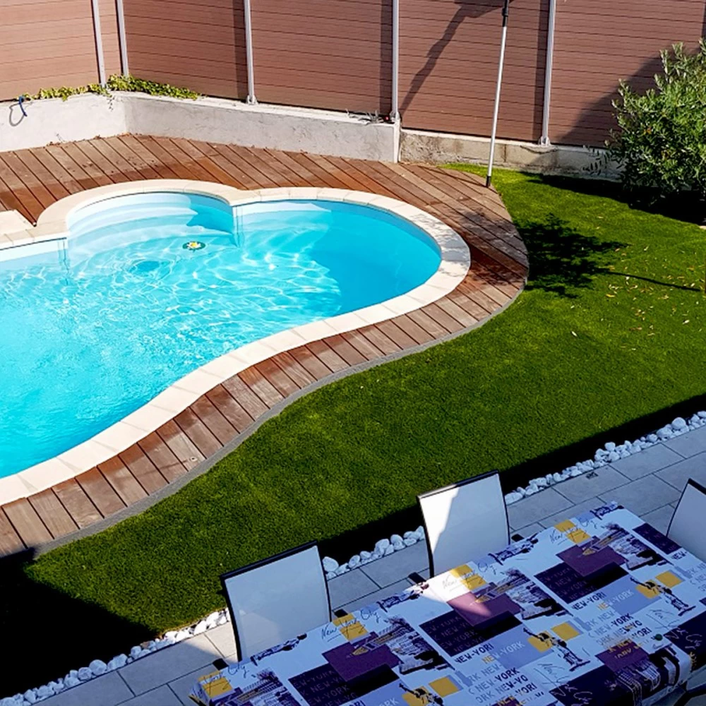 Gazon synthétique entre une piscine courbe, une terrasse en bois et un espace repas